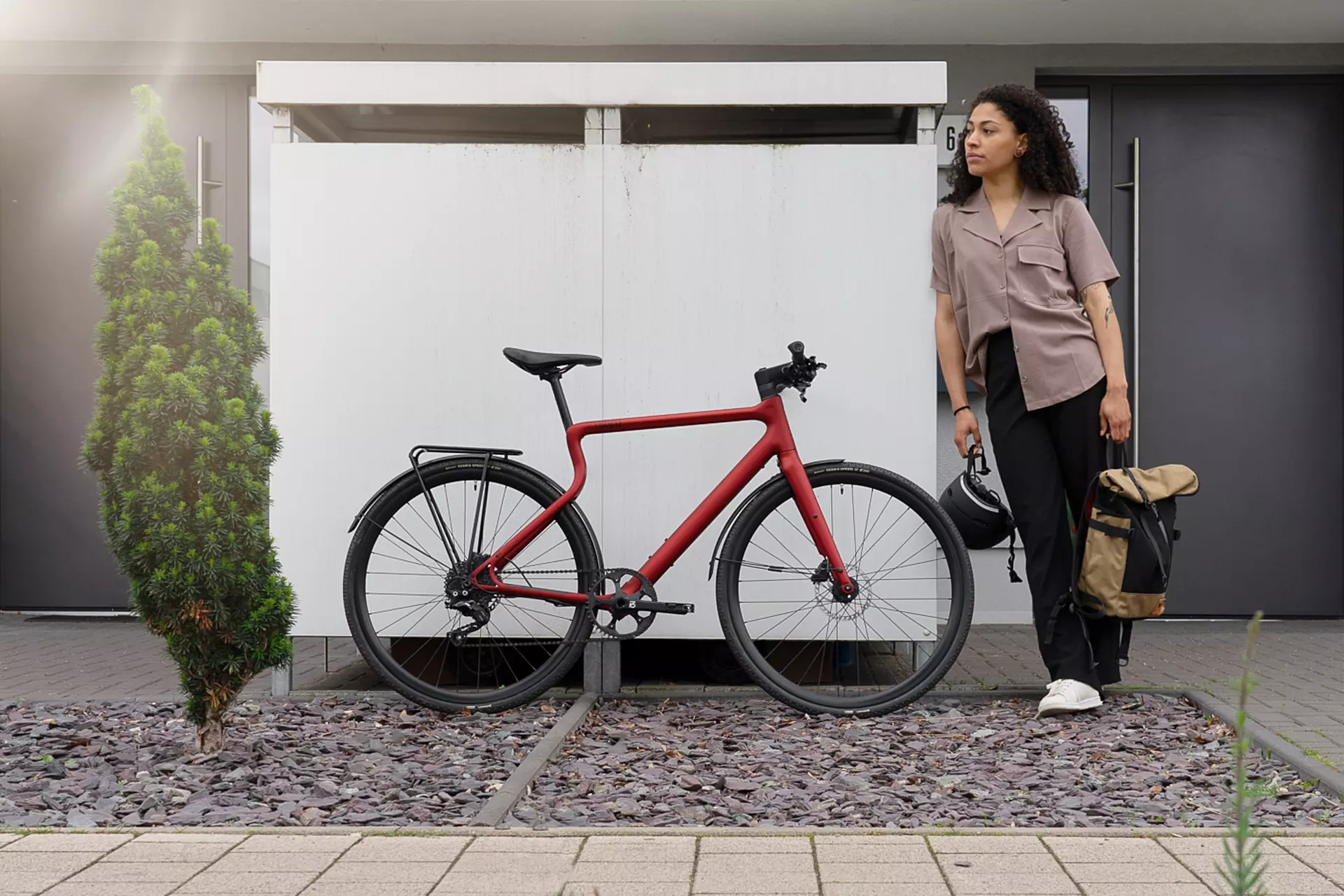 Junge modische Frau steht neben dem oxidfarbenen Urban E-Bikes Stadtfuchs vor einer modernen Stadtvilla