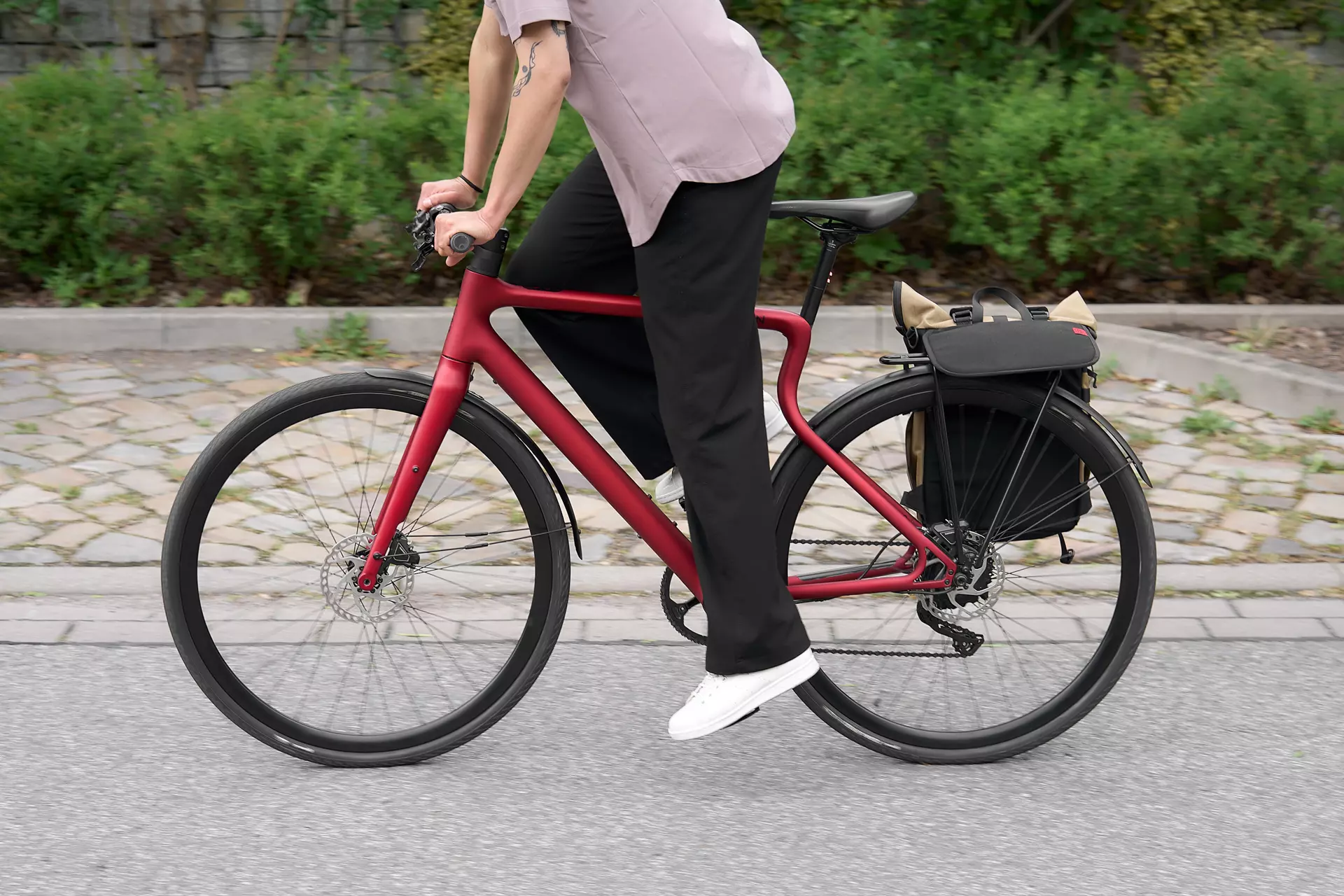 Seitenansicht der Fahrt mit dem E-Bike Stadtfuchs in Oxid Rot mit Saskia, die im Stehen in die Pedale tritt