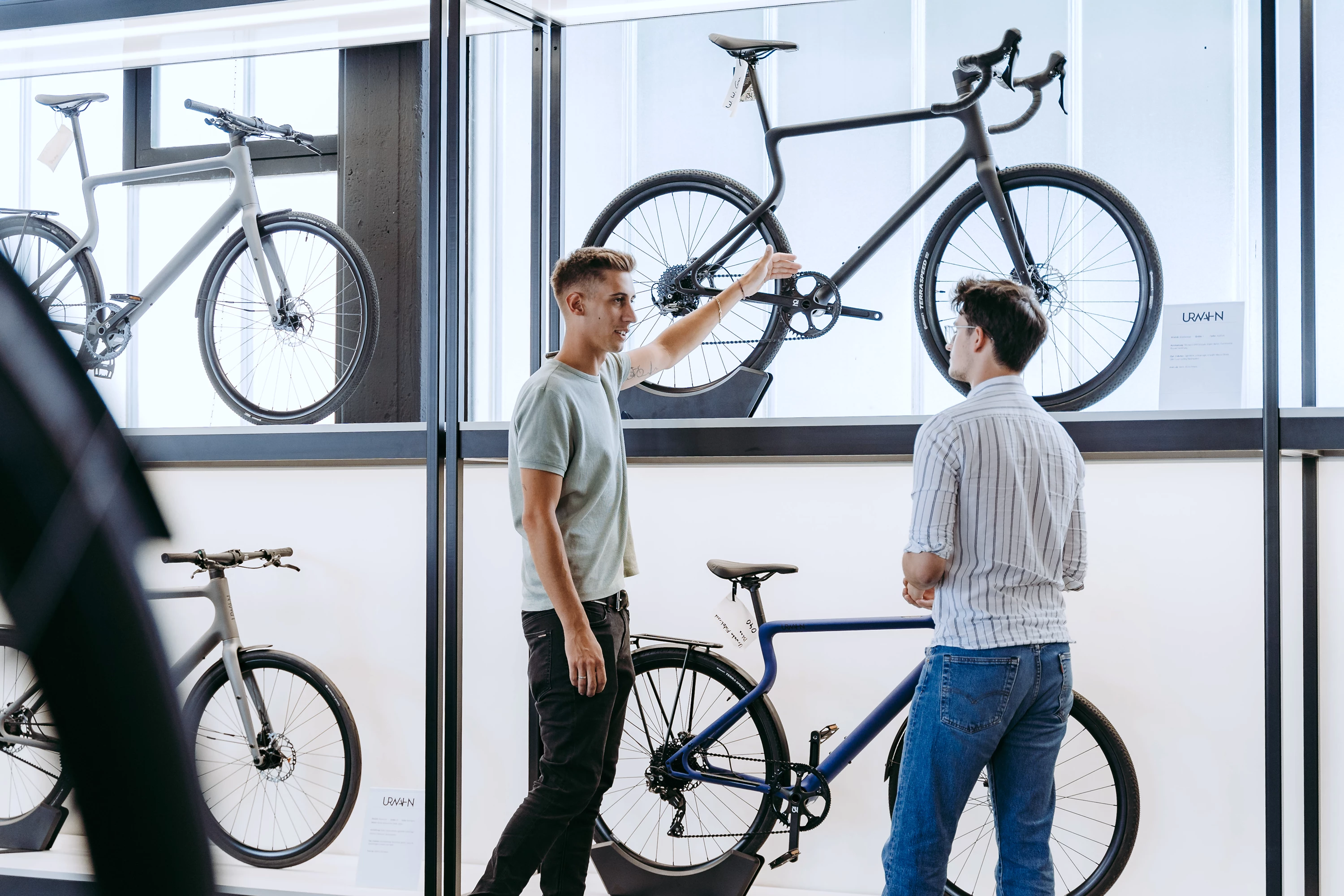 Ein junger Vertriebsmitarbeiter berät einen Kunden mittleren Alters im Urwahn Bike Showroom, im Hintergrund stehen mehrere Urwahn-Fahrräder