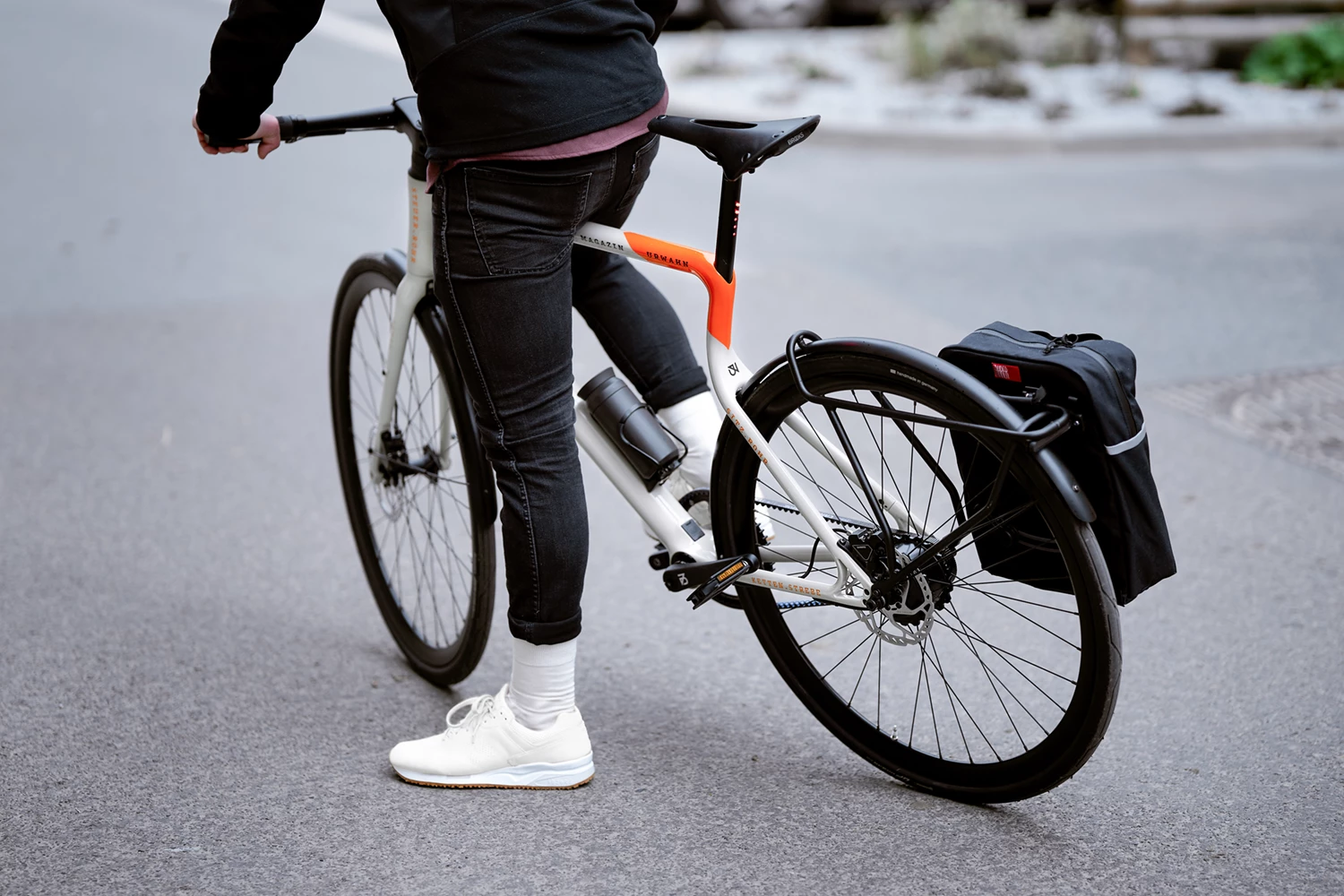 Urban E-Bike Stadtfuchs Magazin Edition steht mit einem Mann auf einem Asphaltuntergrund in Rückansicht