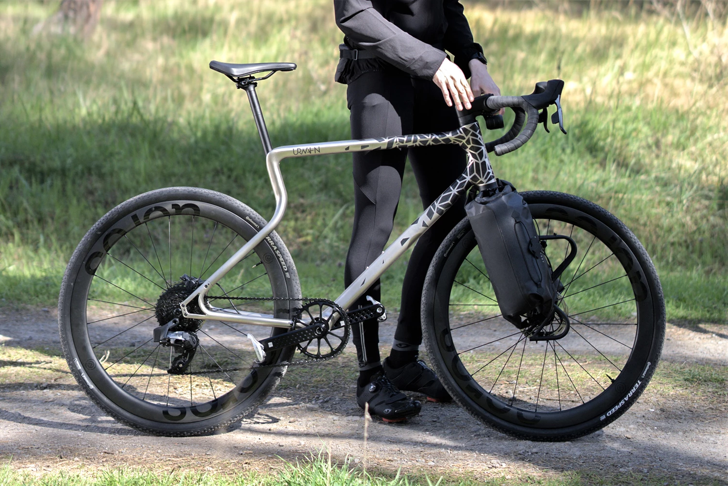 Gravel E-Bike Waldwiesel Acros Edition in Silber mit Lauf Federgabel auf einem Waldweg im Sonnenschein in der Hand eines Mannes