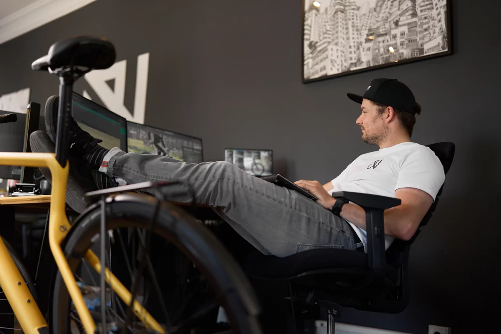Urwahn Mitarbeiter Axel sitzt lässig mit Beinen auf dem Tisch an seinem Arbeitsplatz mit Blick auf den PC-Bildschirm 