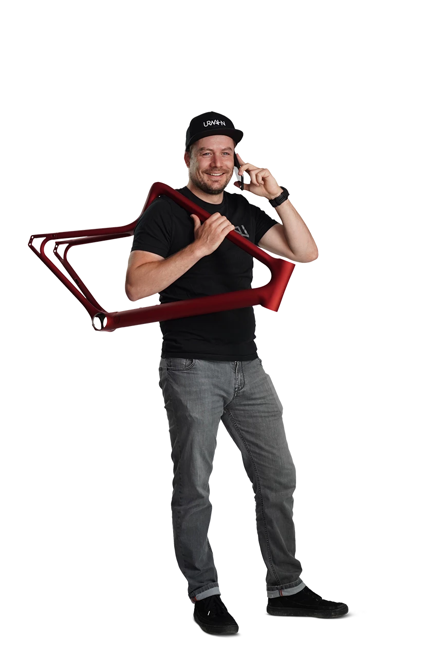 Kundenberater Axel steht und schultert den Urwahn Fahrrad Stahlrahmen in Oxid Rot mit dem Telefon am Ohr