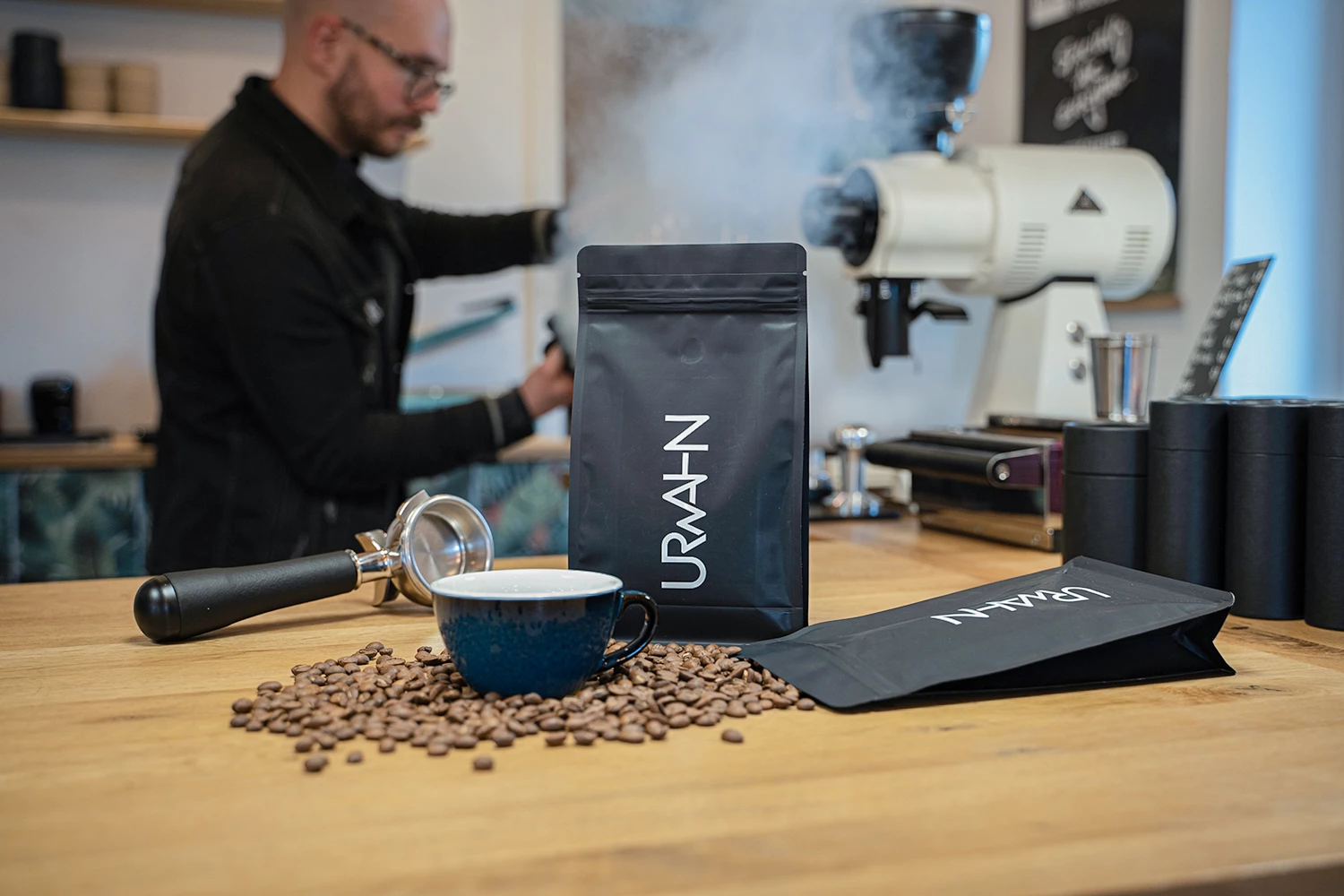 URWAHN Kaffeebohnen sind auf einem Tisch ausgebreitet und im Hintergrund wird Kaffee zubereitet