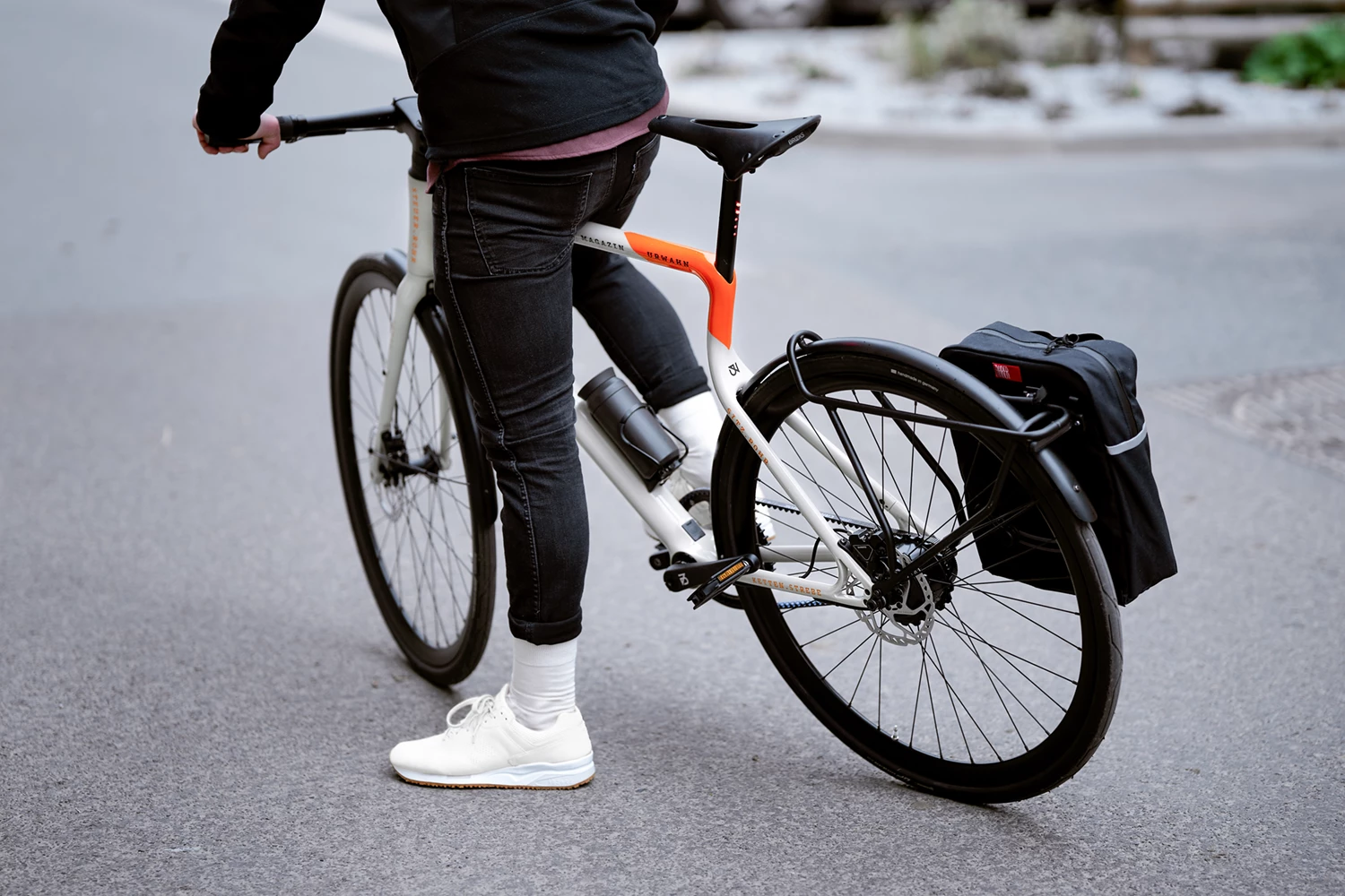 E-Bike Stadtfuchs Magazin Edition steht mit einem Mann auf einem Asphaltuntergrund in Rückansicht